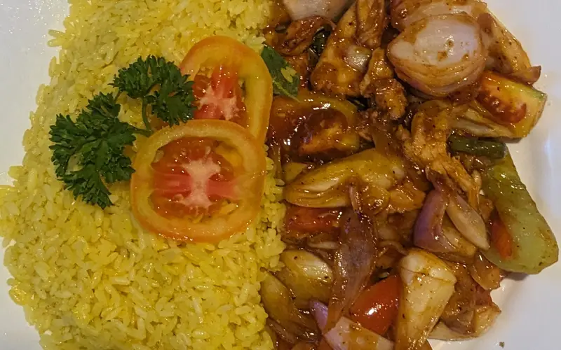 A plate of yellow rice with devilled chicken, peppers and onions